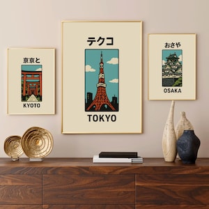 Può includere: Tre stampe incorniciate con illustrazioni di monumenti famosi del Giappone. Le stampe sono in cornici dorate e hanno uno sfondo crema. La stampa superiore presenta una torre rossa e bianca con il testo "Tokyo" e caratteri giapponesi. La stampa centrale presenta un torii rosso con il testo "Kyoto" e caratteri giapponesi. La stampa inferiore presenta un castello con il testo "Osaka" e caratteri giapponesi.
