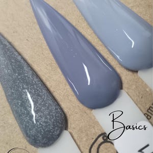 Könnte beinhalten: Drei Nagellack-Farbmuster in Grautönen. Die Farbmuster befinden sich auf einer weißen Oberfläche mit dem Text "Basics" in Schwarz.