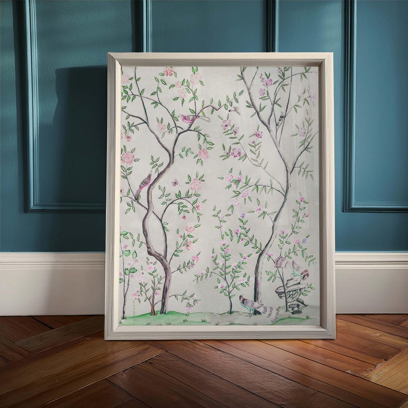 One of the listing’s antique chinoiserie prints of wispy trees with green leaves and pastel-colored blossoms hosting various colorful birds and a butterfly against an off-white background sits in a simple white frame on a vintage wood floor against a muted blue-colored wall.