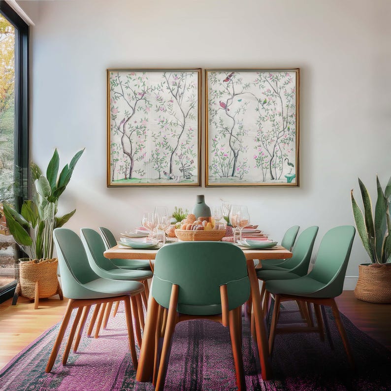 The listing’s pair of antique chinoiserie prints of wispy trees with green leaves and pastel-colored blossoms hosting various colorful birds and a butterfly against a cream background hangs in gold frames above a dining room table with green chairs set for a festive brunch. The light-flooded room also has lush plants and a modern rug.