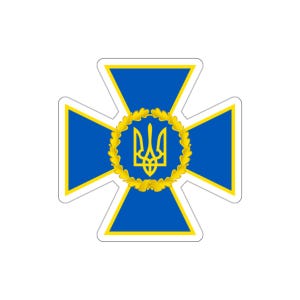 May include: A sticker featuring a blue cross-shaped emblem with a yellow border. The center of the emblem has a gold wreath surrounding a gold trident symbol. The sticker has a white background.
