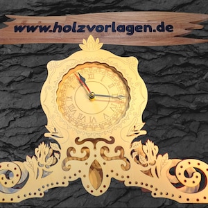 May include: A laser-cut wooden clock with Roman numerals, ornate detailing, and a decorative base. The clock face is visible, and the hands indicate the time. The website www.holzvorlagen.de is displayed on a wooden sign above the clock.