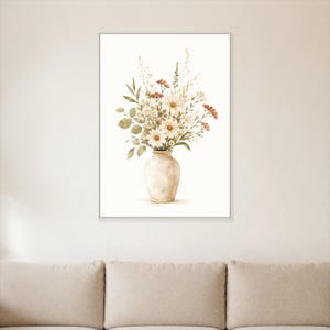 Può includere: Una stampa artistica da parete incorniciata raffigurante un'illustrazione ad acquerello di un bouquet di margherite bianche, fogliame verde e piccoli fiori di campo rosso-marroni in un vaso di ceramica beige chiaro su sfondo bianco.