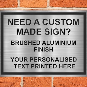 May include: A silver metal sign with black text that reads "Need a custom made sign? Brushed aluminium finish. Your personalised text printed here."
