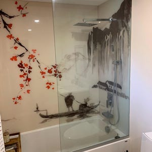 Puede incluir: Una ba&ntilde;era blanca con una mampara de ducha de cristal con un mural de inspiraci&oacute;n asi&aacute;tica. El mural representa un paisaje monta&ntilde;oso, un barco con figuras y detalles florales rojos. Se ven un cabezal de ducha y un grifo.