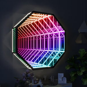 May include: An octagonal wall mirror with a black frame and a vibrant, multicoloured LED light display. The lights transition through a spectrum of colours, creating an illusion of depth and a futuristic aesthetic. The mirror is mounted on a dark grey wall.