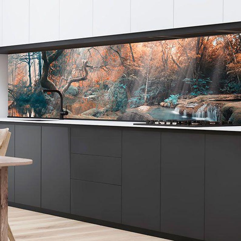 Puede incluir: Un protector contra salpicaduras de cocina con un dise&ntilde;o esc&eacute;nico de bosque y cascada. La imagen presenta una vibrante exhibici&oacute;n de colores oto&ntilde;ales, con un arroyo que fluye a trav&eacute;s del paisaje. Los armarios inferiores son de color gris oscuro con una encimera blanca.