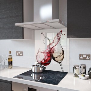 Puede incluir: Un protector contra salpicaduras de cocina con una imagen vibrante de dos copas de vino, una con vino tinto y otra con vino blanco, con salpicaduras de l&iacute;quido. Una olla de acero inoxidable est&aacute; sobre una placa de cocina negra.