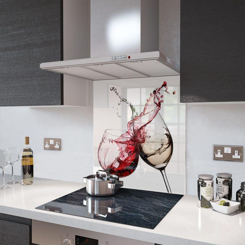 Puede incluir: Un protector contra salpicaduras de cocina con una imagen vibrante de dos copas de vino, una con vino tinto y otra con vino blanco, con salpicaduras de l&iacute;quido. Una olla de acero inoxidable est&aacute; sobre una placa de cocina negra.