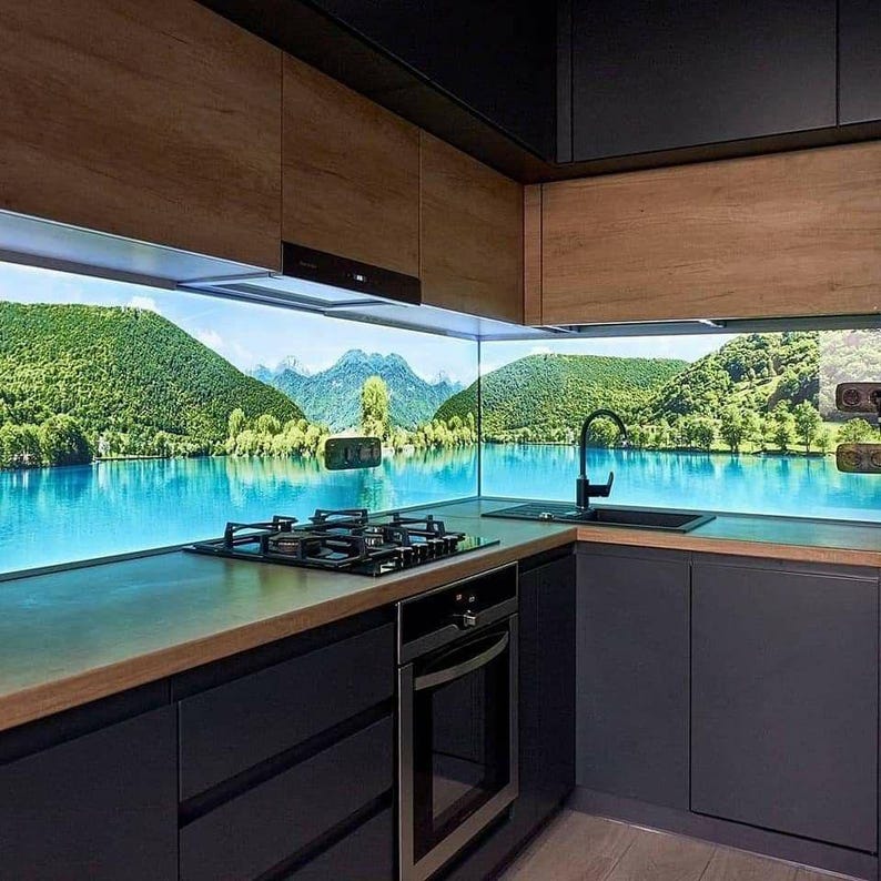 Puede incluir: Dise&ntilde;o de cocina moderno con gabinetes gris oscuro, gabinetes superiores de madera y una encimera con una placa de gas y horno integrados. Un protector contra salpicaduras esc&eacute;nico representa un lago y monta&ntilde;as. Tambi&eacute;n se ve un grifo y un fregadero negros.