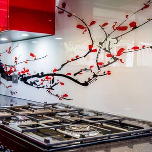 Puede incluir: Una cocina moderna con una estufa de gas negra, una campana extractora roja y un protector contra salpicaduras blanco con un dise&ntilde;o floral negro y rojo. Una tostadora y una tetera de acero inoxidable est&aacute;n en la encimera.
