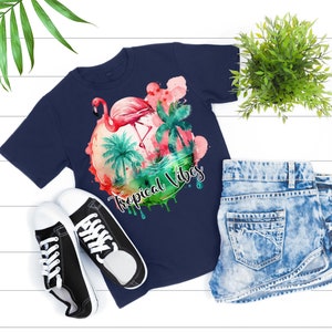 May include: A navy blue t-shirt with a watercolor design of a pink flamingo standing in a tropical scene with palm trees and the text "Tropical Vibes".
