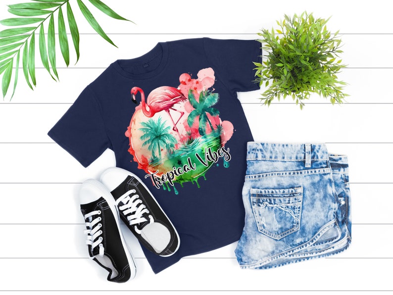 May include: A navy blue t-shirt with a watercolor design of a pink flamingo standing in a tropical scene with palm trees and the text "Tropical Vibes".