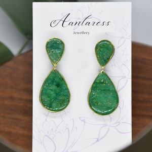 Puede incluir: Un par de pendientes de gota verde y dorado con borde dorado. Los pendientes están en una tarjeta blanca con el texto "Antaress Jewellery".