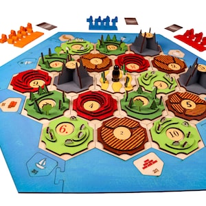 May include: A wooden board game with hexagonal tiles featuring different colored landscapes and numbers. The game board is surrounded by a blue ocean and includes small wooden pieces.