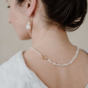 Puede incluir: Una mujer con una camisa blanca y un collar de perlas con un cierre de palanca dorado.