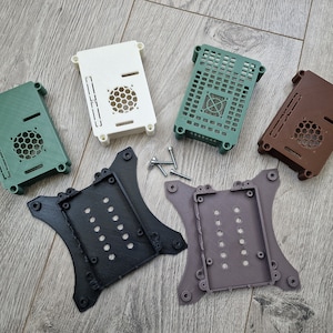 May include: Assortment of six 3D printed Raspberry Pi cases in various colours, including green, white, brown, black, and grey. The cases feature a fan cutout and are designed to fit a Raspberry Pi.