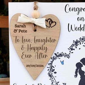 Pu&ograve; includere: Una targa in legno a forma di cuore con un fiocco color crema, una perlina di legno e un testo inciso in marrone scuro che recita Sarah & Pete, To love, laughter & Happily Ever After, e la data 29/09/2026, con due piccoli cuori incisi.