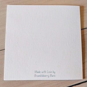 Pu&ograve; includere: Un cartoncino quadrato bianco con una superficie testurizzata. Nella parte inferiore centrale del cartoncino &egrave; presente il testo stampato "Made with Love by Brambleberry Barn" in un semplice carattere sans-serif grigio scuro su fondo bianco.
