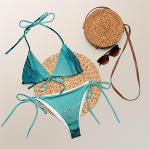 Peut inclure: Un bikini bleu turquoise à imprimé marbré et accents dorés. Le haut du bikini est de style triangle avec des bretelles réglables. Le bas du bikini est de style taille haute avec des liens sur les côtés.