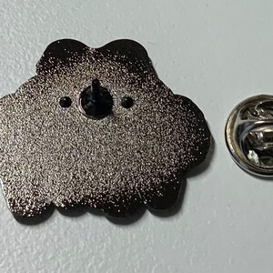 May include: The back of a silver metal pin with a black rubber backing. The pin is shaped like a cloud with a textured surface. The pin has a silver metal clasp.