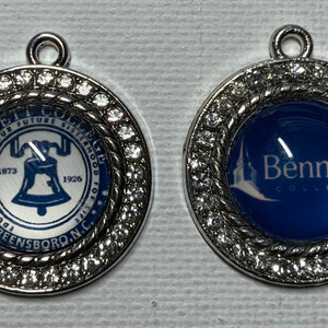 May include: Two silver charms with a white and blue design. One charm features a bell with the text "Bennett College" and the dates "1873" and "1926". The other charm features a blue background with the text "Bennett College" in white.