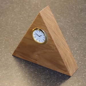 May include: A wooden triangular clock stand with a gold-rimmed clock face. The clock face has Roman numerals and black hands.