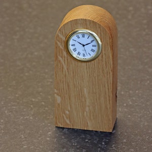 May include: A wooden clock with a gold-coloured face and Roman numeral hour markers. The clock is mounted on a wooden stand with a rounded top.