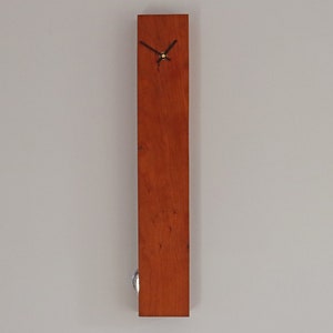 May include: A long, rectangular wooden clock with a simple face and black hands. The clock is stained a rich reddish-brown colour.