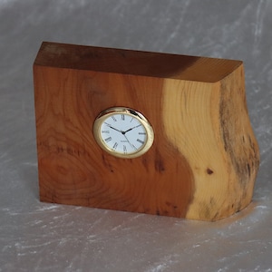 May include: A wooden clock with a gold-coloured frame and white face. The clock is mounted on a natural wood base with a rough-hewn edge.