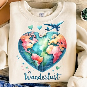 以下が含まれることがあります： クリーム色のスウェットシャツ。水彩画風のデザインで、ハート型の地球儀に青い飛行機とターコイズ色の「Wanderlust」の文字が描かれています。地球儀にはピンク、オレンジ、青の大陸があります。小さなターコイズ色のハートがデザインの周りに散りばめられています。