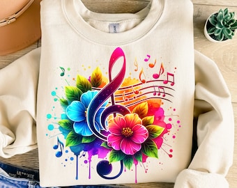 May include: A beige sweatshirt with a colorful watercolor design of a treble clef, musical notes, and flowers. The design is vibrant and includes shades of pink, blue, green, yellow, and orange.