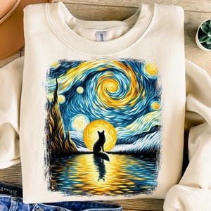 May include: Cream-colored sweatshirt featuring a vibrant, artistic depiction of a fox silhouette against a starry night sky, reminiscent of Van Gogh's style. The design includes swirling blues, yellows, and oranges, with the fox reflected in the water.