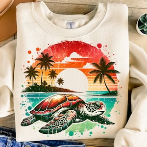 Puede incluir: Una sudadera beige con un gráfico de estilo vintage de una tortuga marina nadando en el océano. El gráfico presenta una puesta de sol con palmeras y un efecto acuarela colorido.