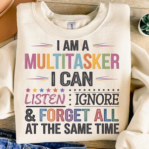 Puede incluir: Una sudadera de color crema con el texto "Soy un multitarea, puedo escuchar, ignorar y olvidar todo al mismo tiempo" en letras de colores.