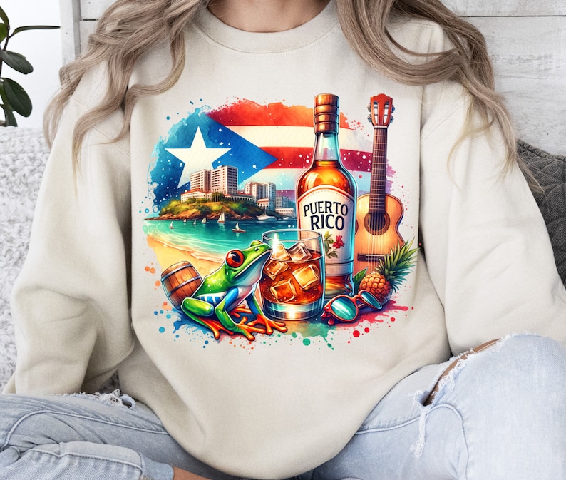 May include: A white sweatshirt with a colourful design featuring a bottle of Puerto Rican rum, a guitar, a frog, and a glass of rum. The design also includes a pineapple, a barrel, and a watercolour-style background.