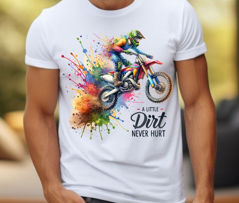 May include: White t-shirt featuring a colorful watercolor illustration of a motocross rider on a dirt bike. The design includes vibrant paint splatters and the text "A Little Dirt Never Hurt."