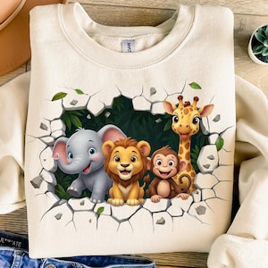 May include: Cream-colored sweatshirt featuring a vibrant illustration of an elephant, lion, monkey, and giraffe emerging from a cracked wall. The cartoon animals are set against a backdrop of green foliage and leaves, creating a playful, whimsical design.