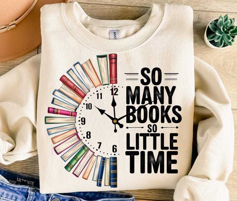K&ouml;nnte beinhalten: Ein cremefarbener Pullover mit einem schwarzen Zifferblatt, das von gestapelten B&uuml;chern umgeben ist. Der Text "=SO= MANY BOOKS SO LITTLE TIME" ist auf dem Pullover aufgedruckt.