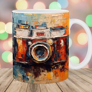 Puede incluir: Taza de cerámica blanca con una pintura impresionista de una cámara vintage. Los colores son naranja, rojo, azul y blanco. La obra de arte tiene un efecto texturizado. La taza tiene un asa estándar y un acabado brillante.