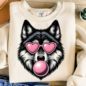 May include: A cream-coloured sweatshirt featuring a black and white wolf wearing pink heart-shaped sunglasses and blowing a pink bubble.