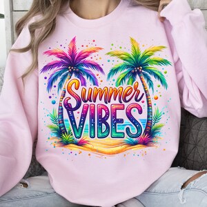 Peut inclure: Sweat-shirt rose avec un motif color&eacute; de deux palmiers et le texte "Summer Vibes".