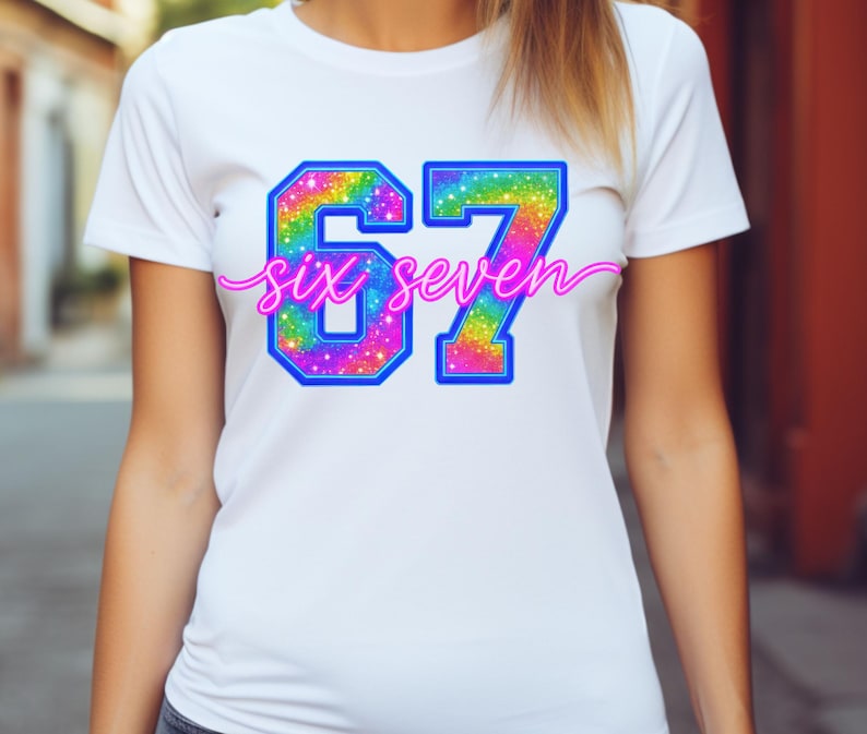 K&ouml;nnte beinhalten: Wei&szlig;es T-Shirt mit einem farbenfrohen, regenbogenfarbenen "67"-Design, umrandet in Blau. Die Worte "six seven" sind in einer kursiven, rosa Schrift &uuml;ber den Zahlen geschrieben.