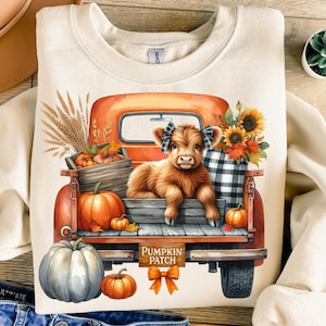 May include: Cream-colored sweatshirt featuring a fall-themed graphic. The graphic depicts a brown Highland cow in the back of an orange vintage truck filled with pumpkins, sunflowers, and the text "Pumpkin Patch".