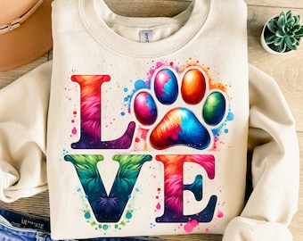 May include: A cream-colored sweatshirt with a colorful "LOVE" graphic. The "O" is replaced with a rainbow paw print. The letters are outlined in black and have a fuzzy texture.