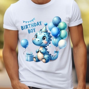 May include: White t-shirt with a blue dinosaur wearing a party hat and holding a gift box. The dinosaur is surrounded by blue and green balloons with a banner that reads "Birthday Boy".