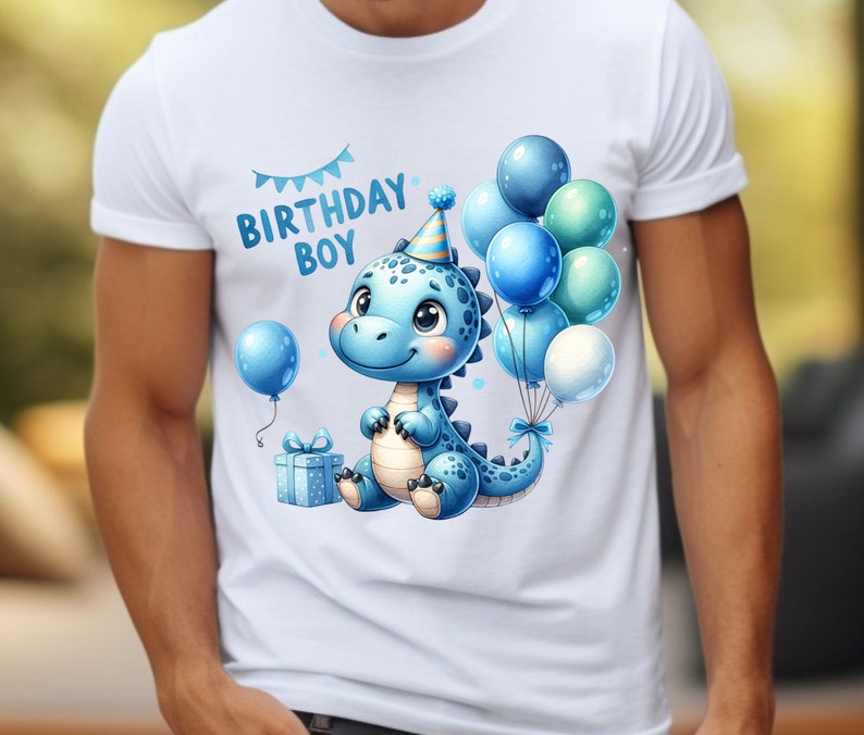 May include: White t-shirt with a blue dinosaur wearing a party hat and holding a gift box. The dinosaur is surrounded by blue and green balloons with a banner that reads "Birthday Boy".