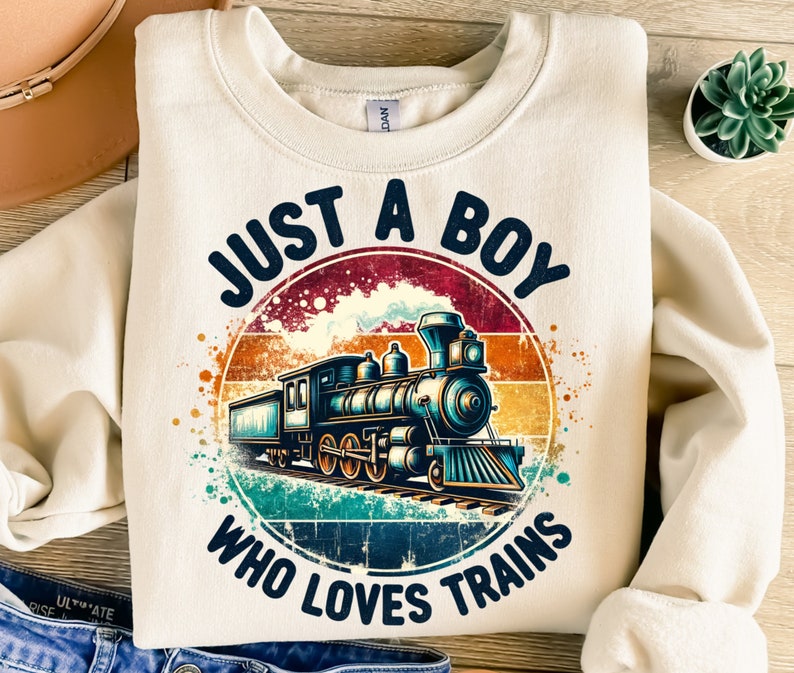 May include: A beige sweatshirt with a vintage-style graphic of a train. The graphic says "Just a Boy Who Loves Trains".