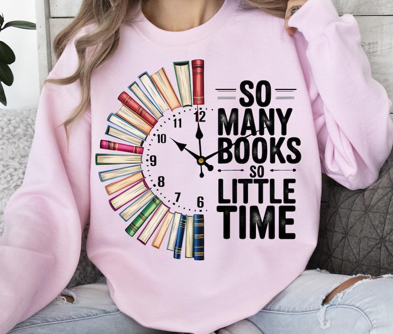 K&ouml;nnte beinhalten: Rosafarbener Pullover mit einem Grafikdruck einer Uhr aus B&uuml;chern. Der Text auf dem Pullover lautet "So many books, so little time."