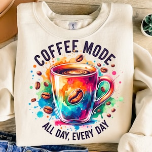 Puede incluir: Una sudadera de color crema con un gráfico de taza de café colorido y el texto "Coffee Mode All Day, Every Day".